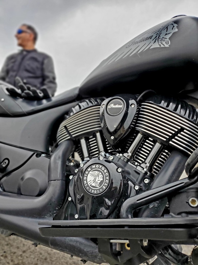 A blacked-out Indian motorcycle with its rider standing behind